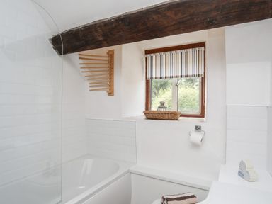 A bathroom with a bathtub and shower area and a window with striped blinds at Gilfachwydd in Islawrdref near Dolgellau