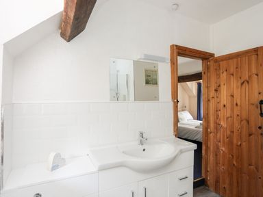 A bathroom with a white sink and mirror next to a wooden door opening to a bedroom at Gilfachwydd in Islawrdref near Dolgellau