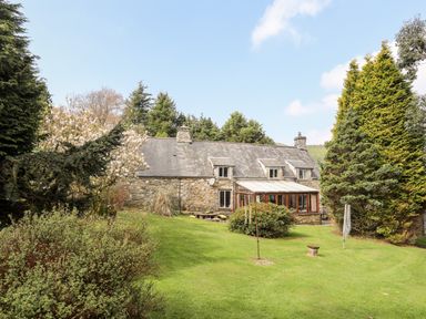 A stone house with a glass conservatory surrounded by trees and grass at Gilfachwydd in Islawrdref near Dolgellau