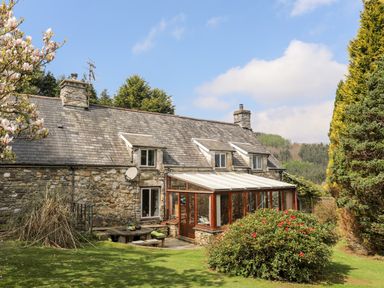 A stone house with a conservatory and garden with trees and shrubs at Gilfachwydd in Islawrdref near Dolgellau
