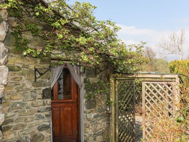 A wooden door set in a stone wall with a lattice gate and climbing plants at Gilfachwydd in Islawrdref near Dolgellau