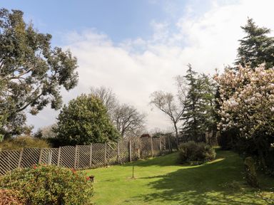 A garden with a lawn fenced by a wooden lattice fence and surrounded by trees and shrubs at Gilfachwydd Islawrdref near Dolgellau