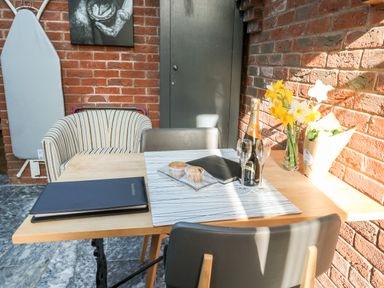 A table with chairs near a brick wall with flowers a bottle of champagne and muffins at Farriers Retreat in Budleigh Salterton