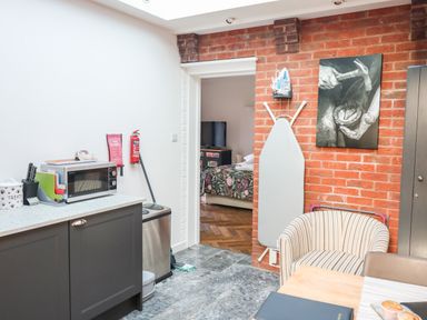 A kitchen area with a microwave on a counter ironing board on a brick wall and a striped chair at Farriers Retreat Budleigh Salterton