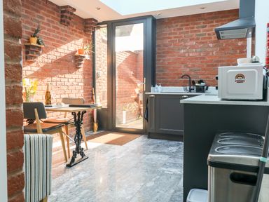 A kitchen with a table and chairs near a glass door and brick walls at Farriers Retreat in Budleigh Salterton