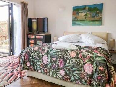 A bedroom with a bed with floral bedspread a television on a cabinet and a painting on the wall at Farriers Retreat in Budleigh Salterton