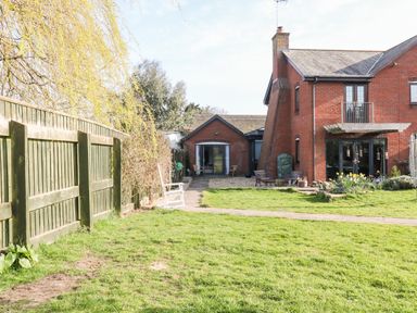 A backyard with green grass a paved path wooden fence and a red brick house with outdoor seating at Farriers Retreat in Budleigh Salterton