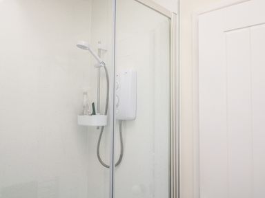 A bathroom shower enclosure with a handheld showerhead and a soap holder containing toiletries at Farriers Retreat in Budleigh Salterton