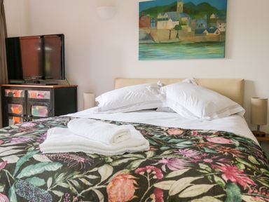 A bedroom with a bed with floral blanket and pillows a TV on a cabinet and a wall painting at Farriers Retreat in Budleigh Salterton