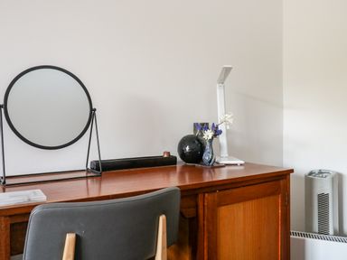 A wooden desk with a round framed mirror a lamp and vases with flowers at Farriers Retreat in Budleigh Salterton