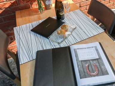 A wooden table with two chairs two muffins on a plate a bottle of prosecco two glasses a vase with flowers and a menu folder showing Farriers Retreat