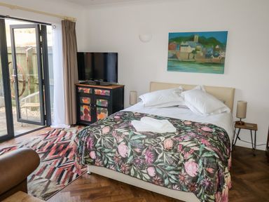 A bedroom with a bed covered in floral blanket a television on a colorful cabinet and a painting on the wall at Farriers Retreat in Budleigh Salterton