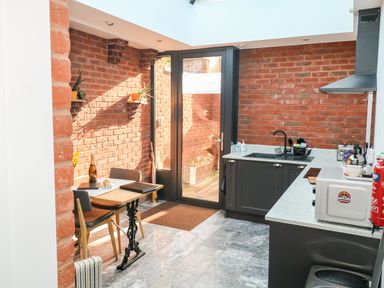 A kitchen with a dining table chairs glass door and brick walls at Farriers Retreat in Budleigh Salterton