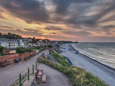A coastal promenade with benches and houses along a pebble beach at sunset at Farriers Retreat Budleigh Salterton