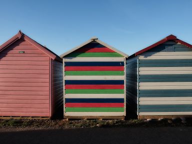Three small wooden beach huts with different colored horizontal stripes at Farriers Retreat in Budleigh Salterton