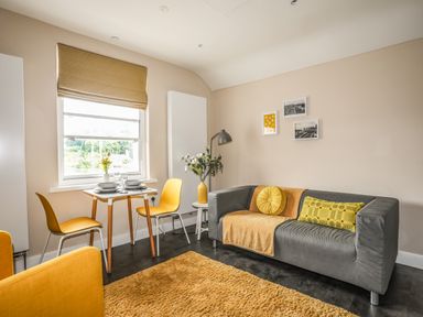 A living room with a grey sofa a yellow rug and a small dining table with two yellow chairs at Cwm Gwyrfai in Caernarfon