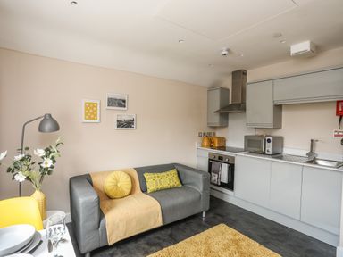 A kitchen and living area with a grey sofa yellow cushions yellow toaster microwave oven and a small dining table at Cwm Gwyrfai in Caernarfon