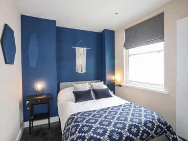 A bedroom with a bed blue and white blanket bedside tables lamps window and blue accent wall at Cwm Gwyrfai in Caernarfon