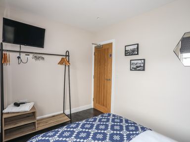 A bedroom corner with a wall-mounted TV wooden door framed pictures and an open clothes rack with hangers at Cwm Gwyrfai in Caernarfon
