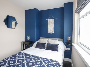 A bedroom with a double bed pillows and a patterned blanket against a blue accent wall with bedside tables and lamps at Cwm Gwyrfai in Caernarfon