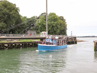 A blue boat named Queen of the Sea with passengers on water near a bridge and trees at Cwm Gwyrfai in Caernarfon