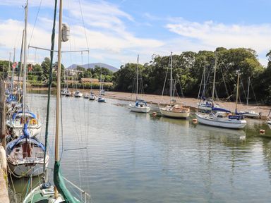 A river with sailboats moored near the shore with trees and buildings in the background at Cwm Gwyrfai in Caernarfon