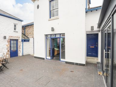 A courtyard with white walls blue doors and outdoor wooden tables and chairs at Moel Tryfan in Caernarfon