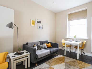 A living room with a gray sofa yellow chairs a white dining table a floor lamp and a small plant on tables at Moel Tryfan in Caernarfon