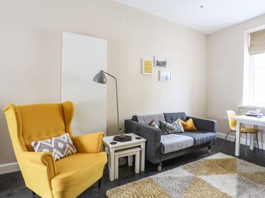 A living room with a yellow armchair a gray sofa with cushions white nesting tables and a dining table at Moel Tryfan in Caernarfon