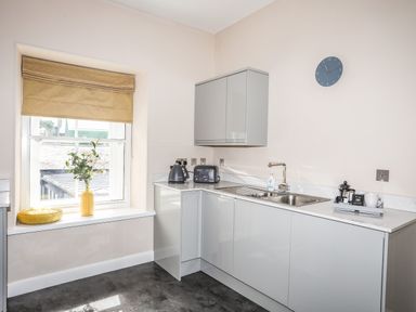 A kitchen with a window seat with a yellow cushion and vase with flowers a kettle toaster sink and wall clock at Moel Tryfan in Caernarfon