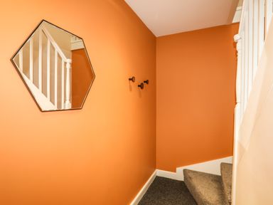 A staircase with orange walls a hexagonal mirror and three black hooks at Moel Tryfan in Caernarfon