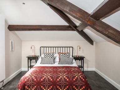 A bedroom with a double bed with pillows and patterned blanket under wooden ceiling beams at Moel Tryfan in Caernarfon