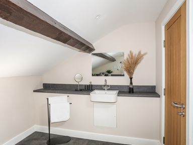 A bathroom sink with a mirror above a dark countertop and a towel rack with white towels in a room with a wooden door and exposed ceiling beam at Moel Tryfan in Caernarfon