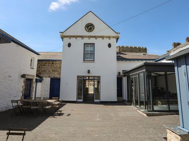 An outdoor courtyard with tables and chairs in front of a white building with a clock at Moel Tryfan in Caernarfon