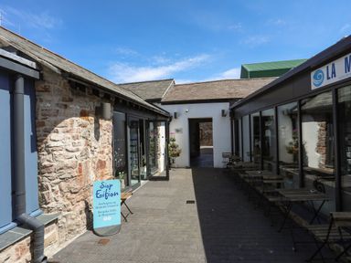 An outdoor walkway between stone and glass buildings with tables and chairs at Moel Tryfan in Caernarfon