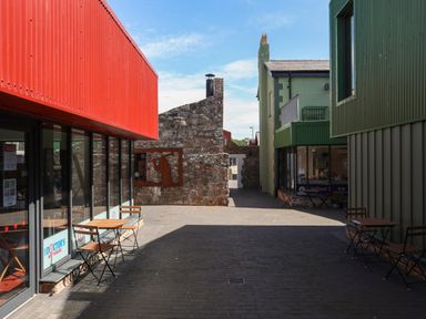 An outdoor seating area with tables and chairs between buildings with red and green metal siding at Moel Tryfan in Caernarfon