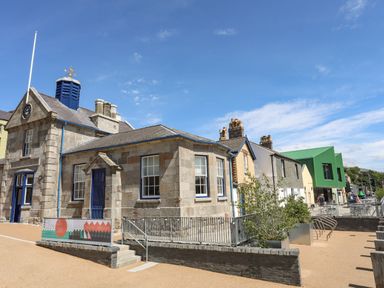 An outdoor area with a stone building with a clock tower and a blue door next to other buildings and outdoor seating