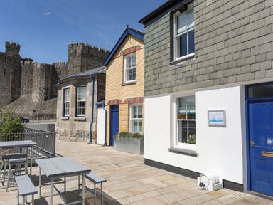 An outdoor seating area with tables and benches next to a row of buildings with a castle in the background at Moel Tryfan in Caernarfon