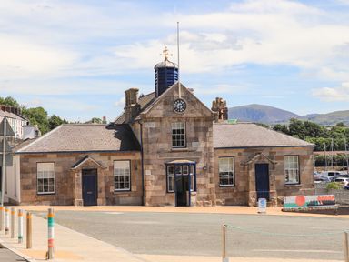 A stone building with a clock tower and blue doors along a paved street at Moel Tryfan in Caernarfon