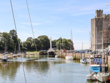 A harbor with boats docked along the water and a stone castle tower in Caernarfon