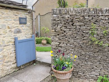 A stone wall with a blue wooden gate and a planter with flowers at Manor Cottage in Poulton