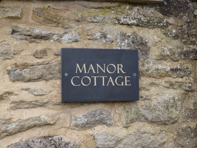 A stone wall with a sign reading Manor Cottage at Manor Cottage in Poulton