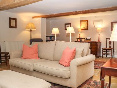 A living room with a beige sofa with pink pillows and multiple lamps at Manor Cottage in Poulton