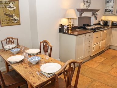 A kitchen with wooden dining table set for four and cream cabinets with stove at Manor Cottage in Poulton