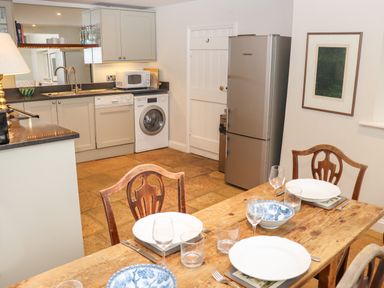 A kitchen with dining table set for four next to a fridge washing machine and dishwasher at Manor Cottage in Poulton