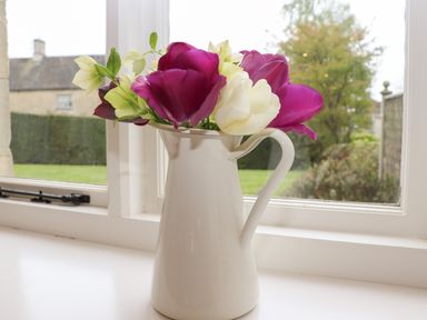 A white pitcher with purple and white flowers on a windowsill with a garden outside at Manor Cottage in Poulton