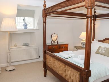 A bedroom with a four-poster bed towels on bed a wooden chest of drawers mirror lamps and a window at Manor Cottage in Poulton