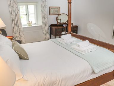 A bedroom with a wooden bed covered in white linens and towels on a folded blanket near a window with curtains and a wooden dressing table at Manor Cottage in Poulton