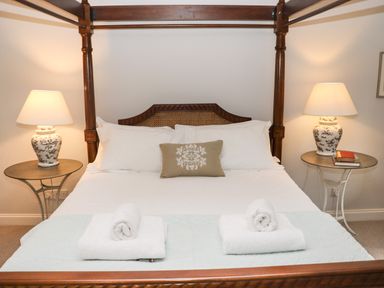 A bedroom with a wooden four-poster bed white bedding two rolled towels on the bed two bedside tables with matching lamps and books at Manor Cottage in Poulton