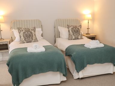 A bedroom with two single beds each with a pillow a folded towel and a green blanket and two bedside tables with lamps at Manor Cottage in Poulton